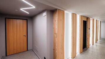 Un couloir aux murs recouverts de lambris en bois, une porte fermée et un plafond doté de luminaires linéaires.