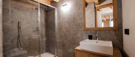 A modern bathroom with a glass-enclosed shower, a wooden vanity, and a large mirror.