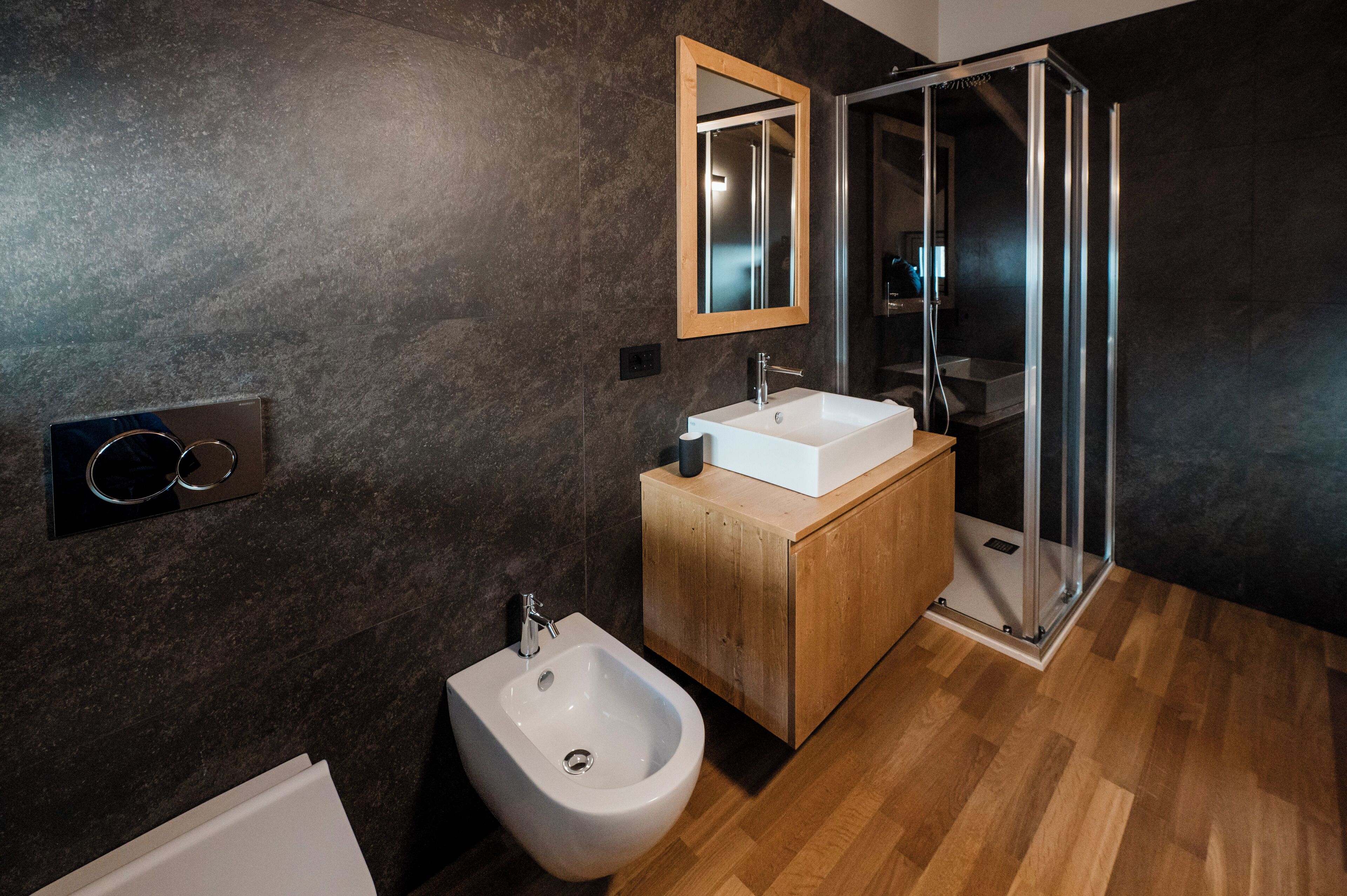 Un baño moderno con tocador de madera, lavamanos blanco, bidé, cabina de ducha de vidrio y espejo en la pared.