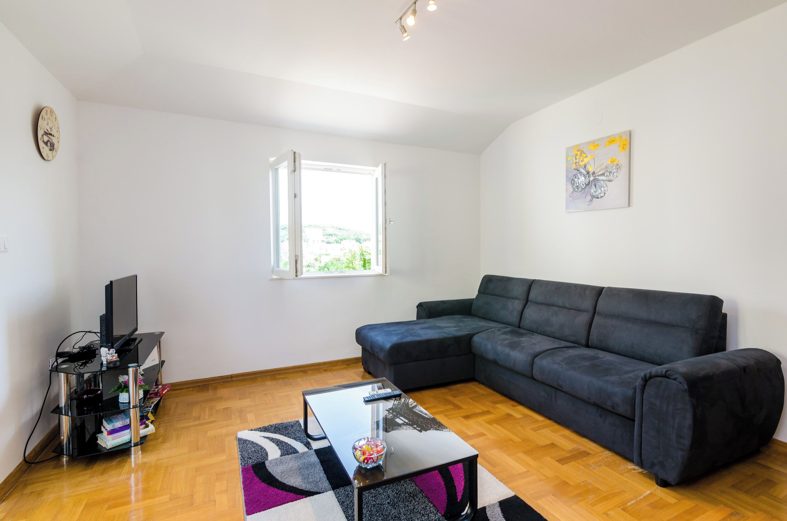 A modern living room with a black sofa, a glass coffee table, and a TV stand with books and decorative items.