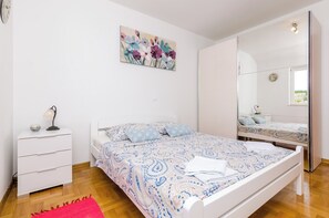 A bedroom with a bed, a nightstand, a lamp, a mirror, and a painting on the wall. - Ana Apartment (Konavle)