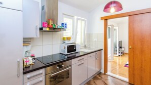 A modern kitchen with white cabinets, a microwave, and a wooden door leading to a living area. - Ana Apartment (Konavle)
