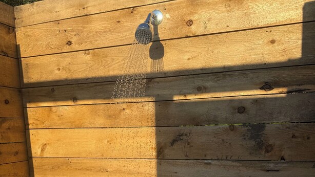 A wooden shower enclosure with a showerhead and two faucets. - Throw your tent anywhere! (Westmore)