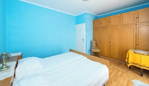Un dormitorio con cama, armario de madera, una silla y una pequeña mesa con mantel amarillo.