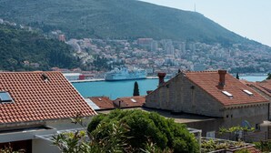 A coastal cityscape with a prominent ship docked at the harbor, surrounded by residential buildings with red-tiled roofs.
