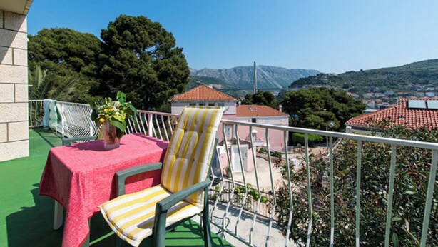 A balcony with a table and chairs, a potted plant, and a view of a town and mountains.