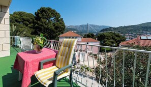 A balcony with a table and chairs, a potted plant, and a view of a town and mountains. - Guest House Mrdalo (Dubrovnik)