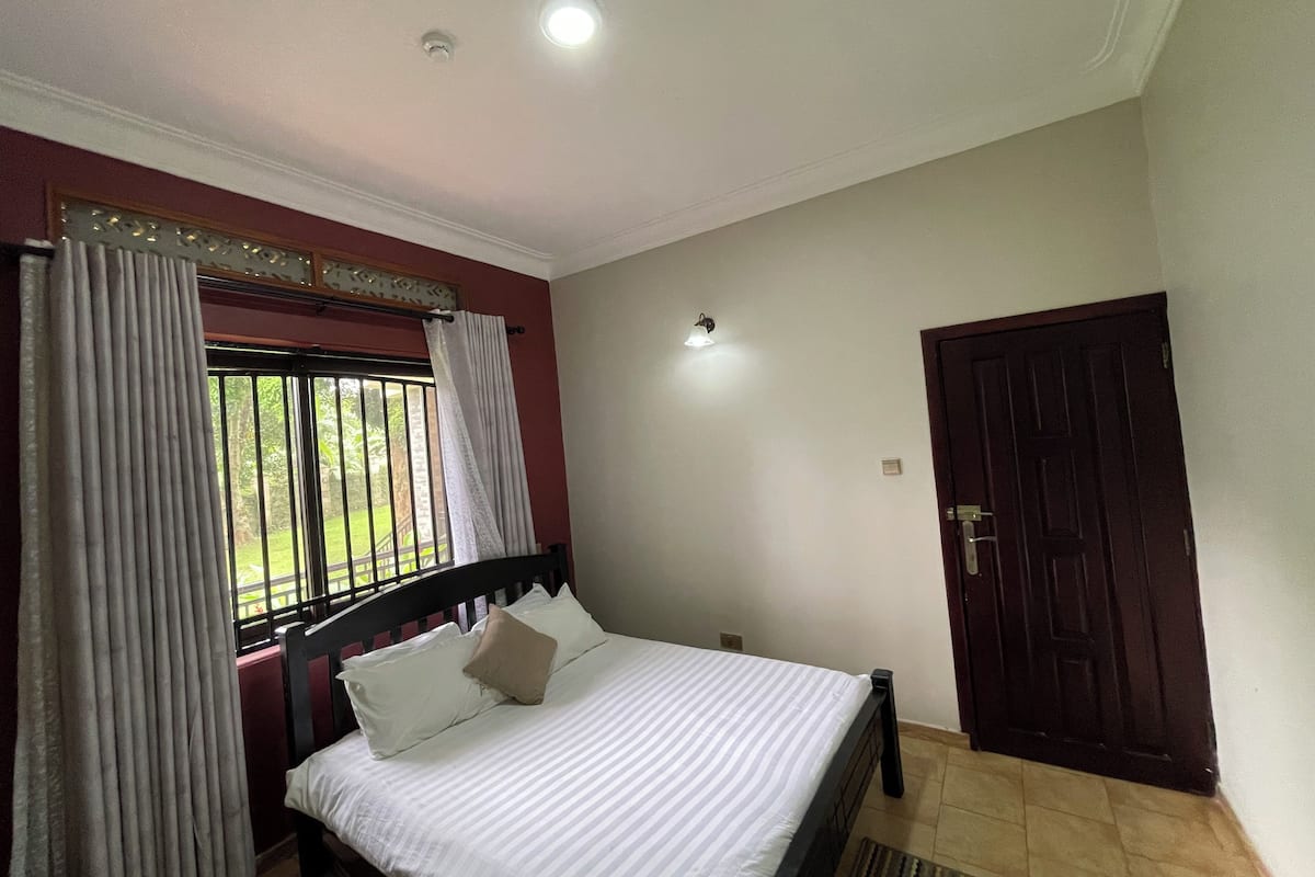 A bedroom with a bed, curtains, a window, a door, and a light fixture.