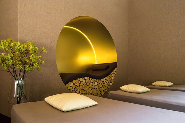 Ein Wellnessraum mit einem großen Spiegel, einer Vase mit Grünpflanzen und zwei Massagetischen mit Kissen.