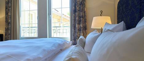 Habitación de hotel con una cama grande, dos ventanas con cortinas, una lámpara y vistas al exterior.