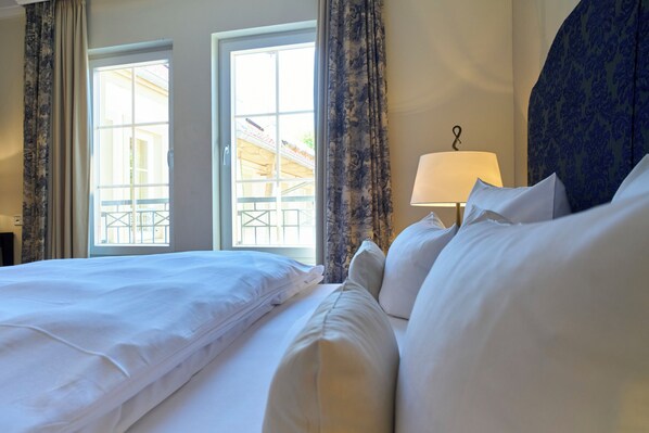 Habitación de hotel con una cama grande, dos ventanas con cortinas, una lámpara y vistas al exterior.