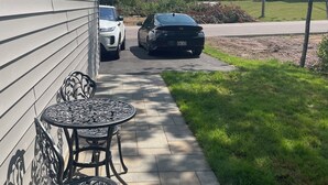 Eine Terrasse mit Tisch und Stühlen, ein Weg und zwei geparkte Autos.