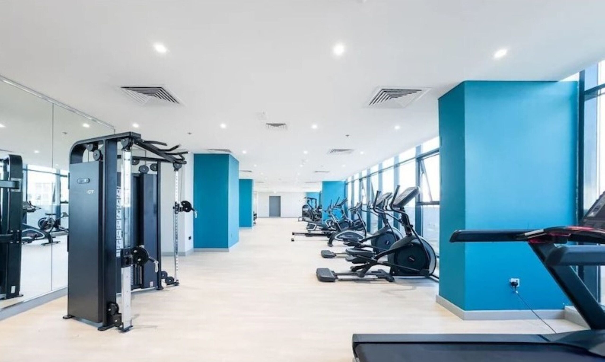 Une salle de sport moderne équipée de machines de cardio, d’appareils de musculation et dotée de grandes fenêtres.