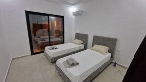 Ein Hotelzimmer mit zwei Einzelbetten, einer Schiebeglastür, die auf einen Balkon führt, und einer Decken-Klimaanlage.