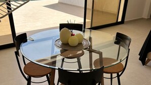 Ein Esstisch mit Glasplatte und vier Stühlen, ein kleiner runder Tisch mit Dekoration sowie Blick auf einen Garten und ein Gebäude.
