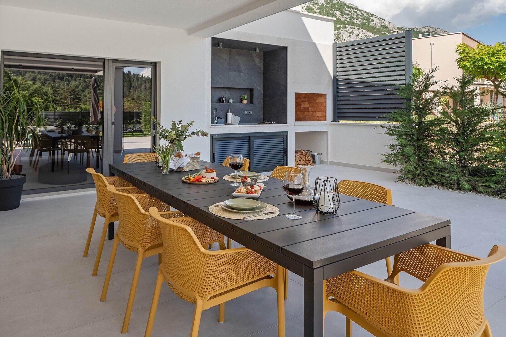 An outdoor dining area with a long table set for a meal, surrounded by wicker chairs.