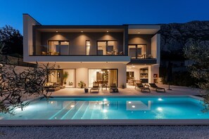 Ein modernes, zweistöckiges Haus mit Schwimmbad, Sitzgelegenheiten im Freien und einer gut beleuchteten Terrassenfläche.