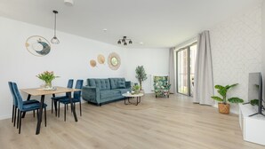 Una sala de estar moderna con un sofá azul, una mesa de comedor con sillas, una mesa de centro y un mueble para televisor.