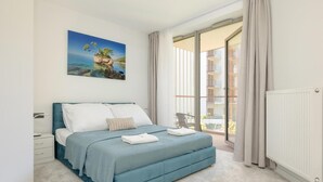 Un dormitorio con cama, mesita de noche, ventana con cortinas y vista a un balcón.