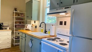 Una cocina con estufa blanca, un fregadero y un refrigerador. Hay una repisa con frascos y una cafetera.