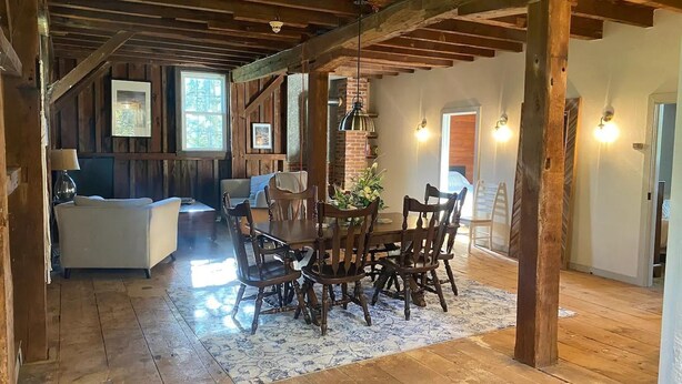 Un comedor rústico con una mesa y sillas de madera, un tapete estampado y vigas de madera a la vista.