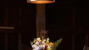 Una mesa con un jarrón de flores y una lámpara colgante.