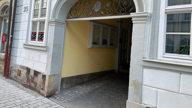A building entrance with a yellow wall, a decorative metal archway, and a sign with the year 1780. - Design-ferienwohnung Altstadtperle Mitten im Zentrum von Hildburghausen (Hildburghausen)