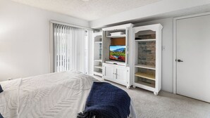 A bedroom with a bed, a TV on a white entertainment unit, and a wardrobe.