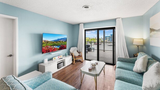 A modern living room with a flat-screen TV, a sofa, a coffee table, and a balcony with a view of the city.