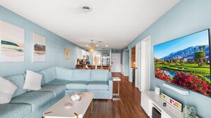 A modern living room with a light blue sofa, a coffee table, and a flat-screen TV displaying a scenic landscape.