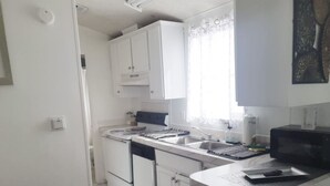Pieni, käytännöllinen keittiö, jossa on valkoiset kaapit, liesi, mikroaaltouuni ja pesuallas.