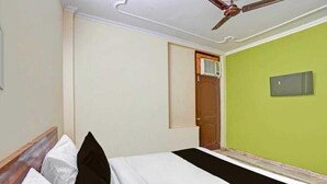 A hotel room with a bed, a ceiling fan, a door, and a green wall. - JPS LUX RESIDENCY (New Delhi)