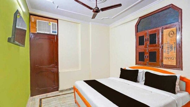 A bedroom with a bed, a ceiling fan, a wooden door, and a window with a wooden frame. - JPS LUX RESIDENCY (New Delhi)