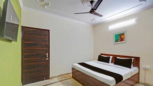 A bedroom with a bed, a ceiling fan, a door, and a wall-mounted TV. - JPS LUX RESIDENCY (New Delhi)
