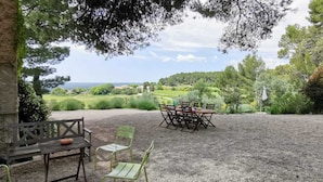 An outdoor seating area with a table and chairs, overlooking a scenic landscape with trees and a view of the sea. - Maison Familiale à Aix en Provence, au Calme, vue Magnifique (Aix-en-Provence)