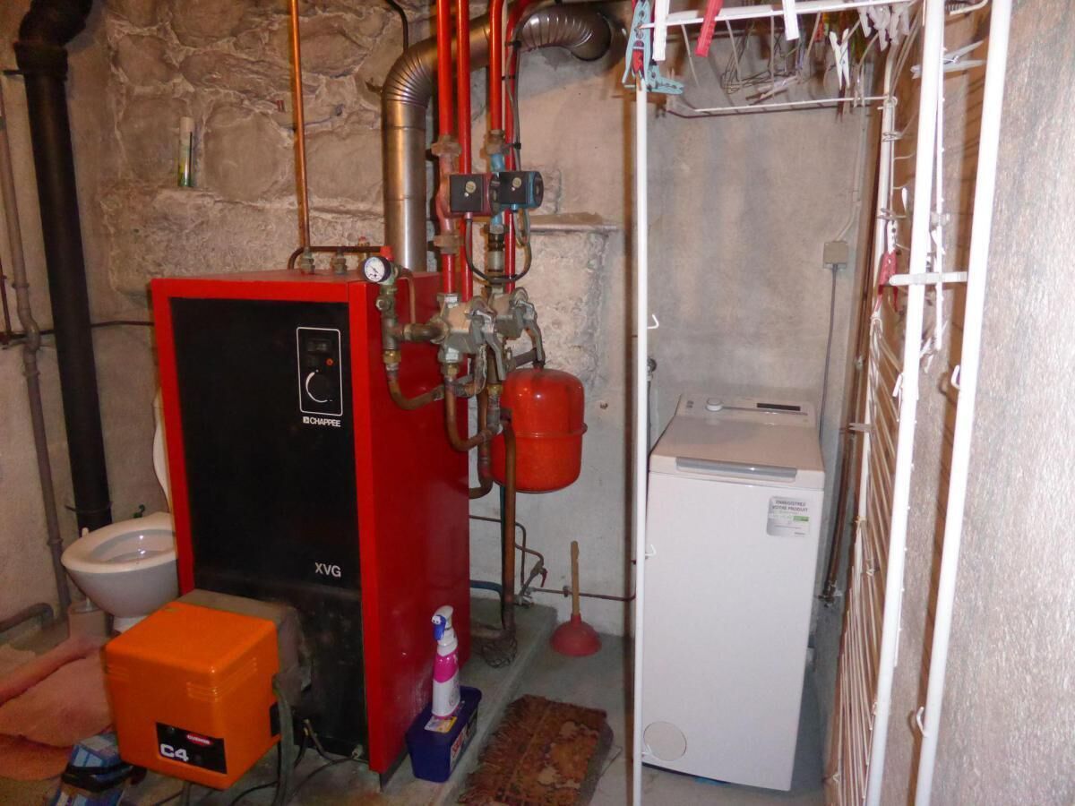 A compact bathroom with a red water heater, a white toilet, and a small white refrigerator.