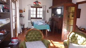 Un comedor con una mesa preparada para cuatro personas, un sillón verde y una mesa de madera con mantel azul.