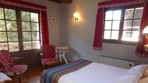 Un dormitorio con una cama grande, dos sillones, una mesita y un ventanal con cortinas.