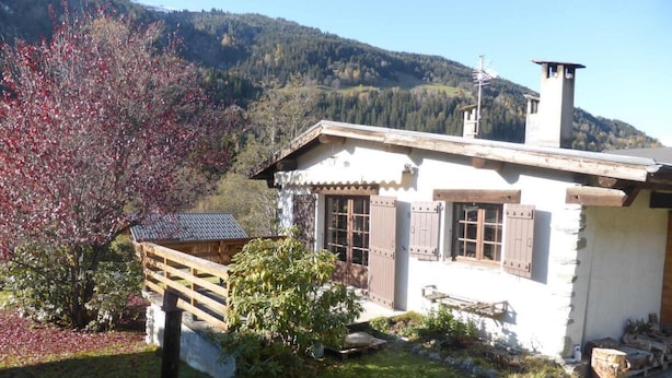 Una cabaña rústica con terraza de madera, chimenea de piedra y vistas a la montaña.