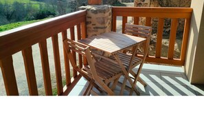 Een houten terras met een tafel en stoelen, een stenen muur en uitzicht op het landschap.