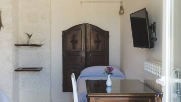 Una habitación con una cama, una mesa de madera con un florero, una silla, un televisor montado en la pared y un radiador.