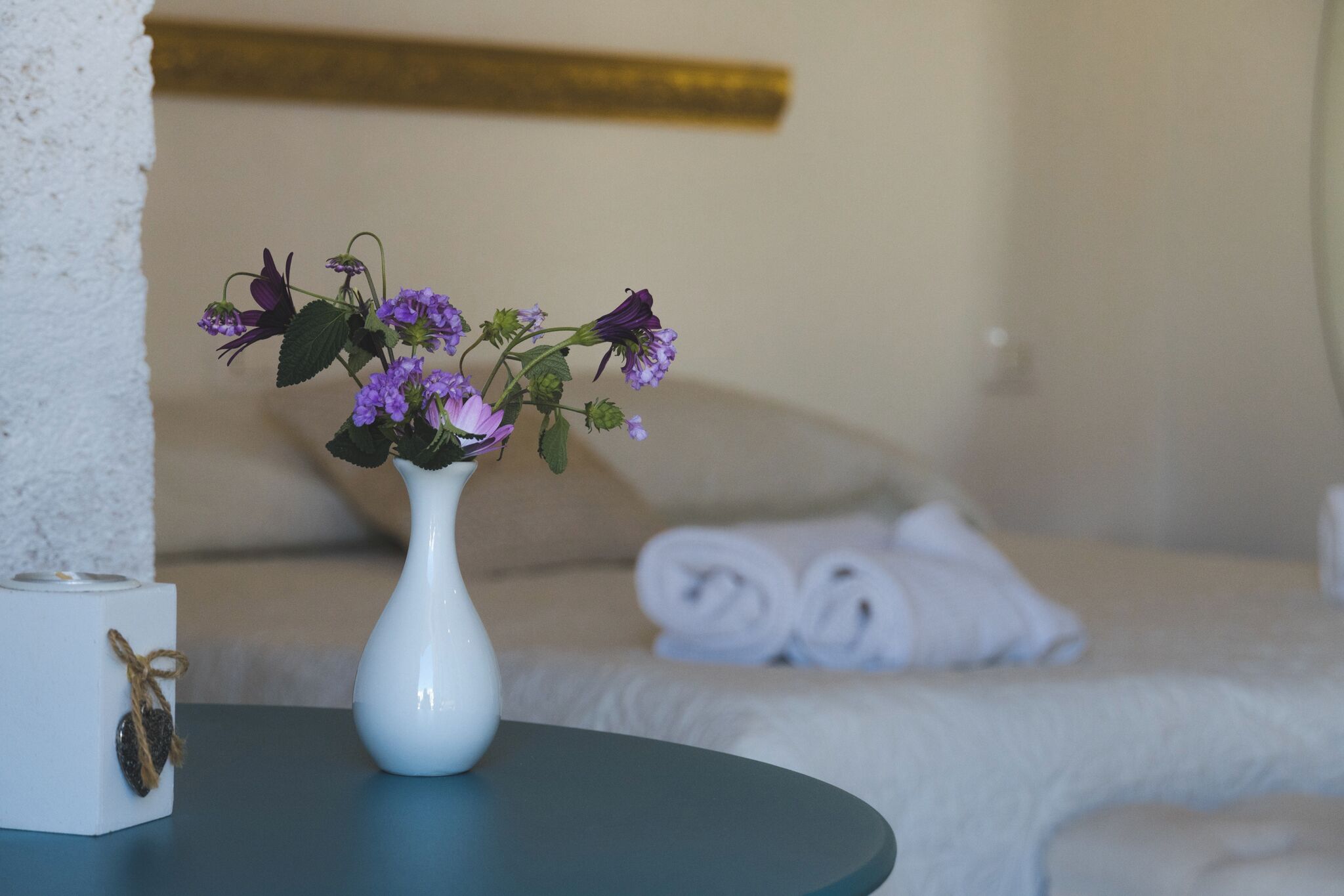 Een witte vaas met paarse bloemen op een tafel in een hotelkamer.
