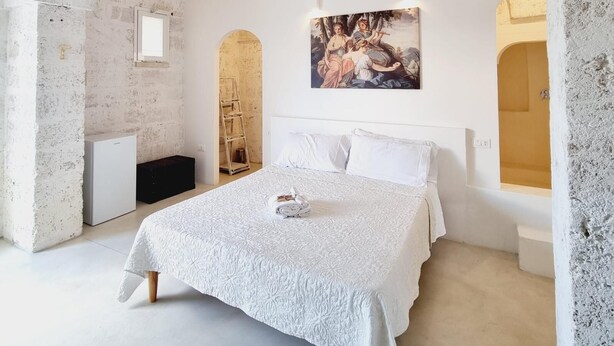 A bedroom with a large bed, a painting on the wall, and a stone ceiling. - Corte Mercurio Beb (Ugento)