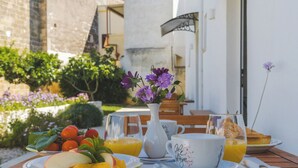 A breakfast table with plates of fruit, a vase of flowers, and glasses of orange juice. - Corte Mercurio Beb (Ugento)