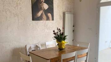 Een eethoek met een houten tafel en witte stoelen, een schilderij aan de muur, en een radiator.