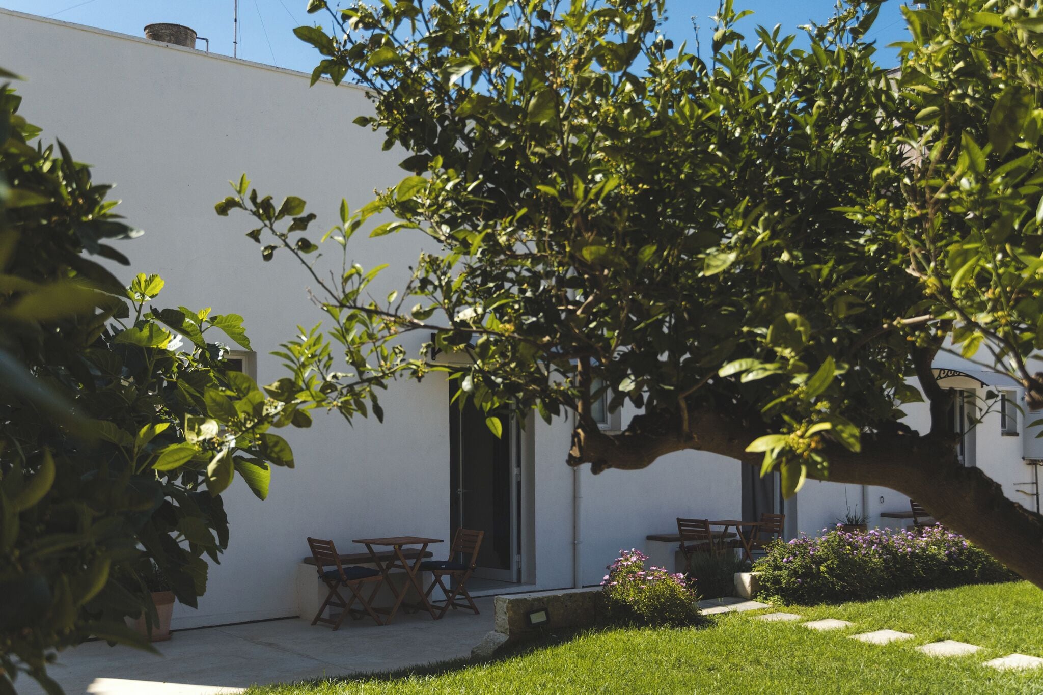 Un edificio blanco con un patio amoblado, incluyendo mobiliario exterior y un árbol.