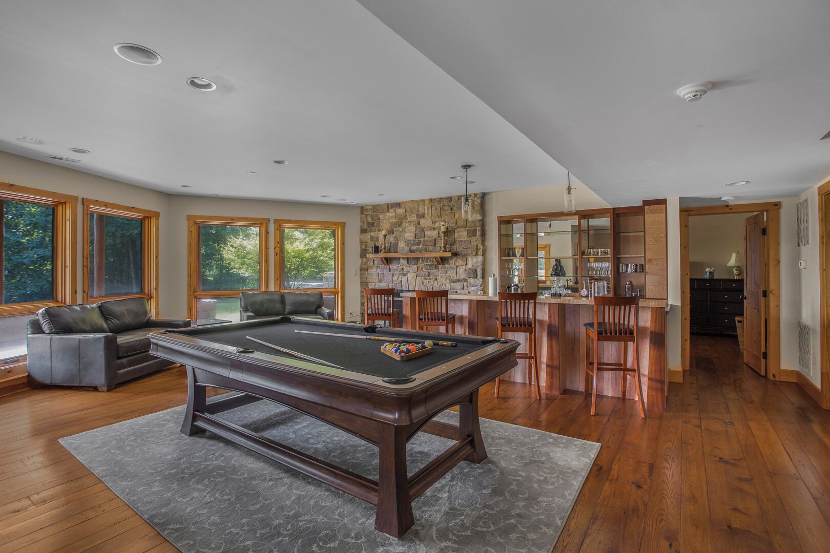 Un vaste salon comprenant une table de billard, un coin bar et un mur décoratif en pierre.