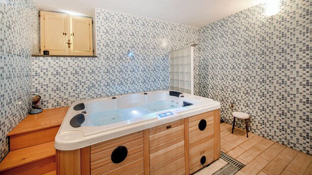 A bathroom with a wooden bathtub, tiled walls, a wooden vanity, and a small stool. - Hotel Solcalante (Procida)