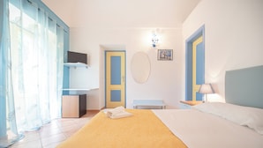 A hotel room with a bed, a bedside table, a lamp, a TV, and a bathroom with a shower curtain. - Hotel Solcalante (Procida)