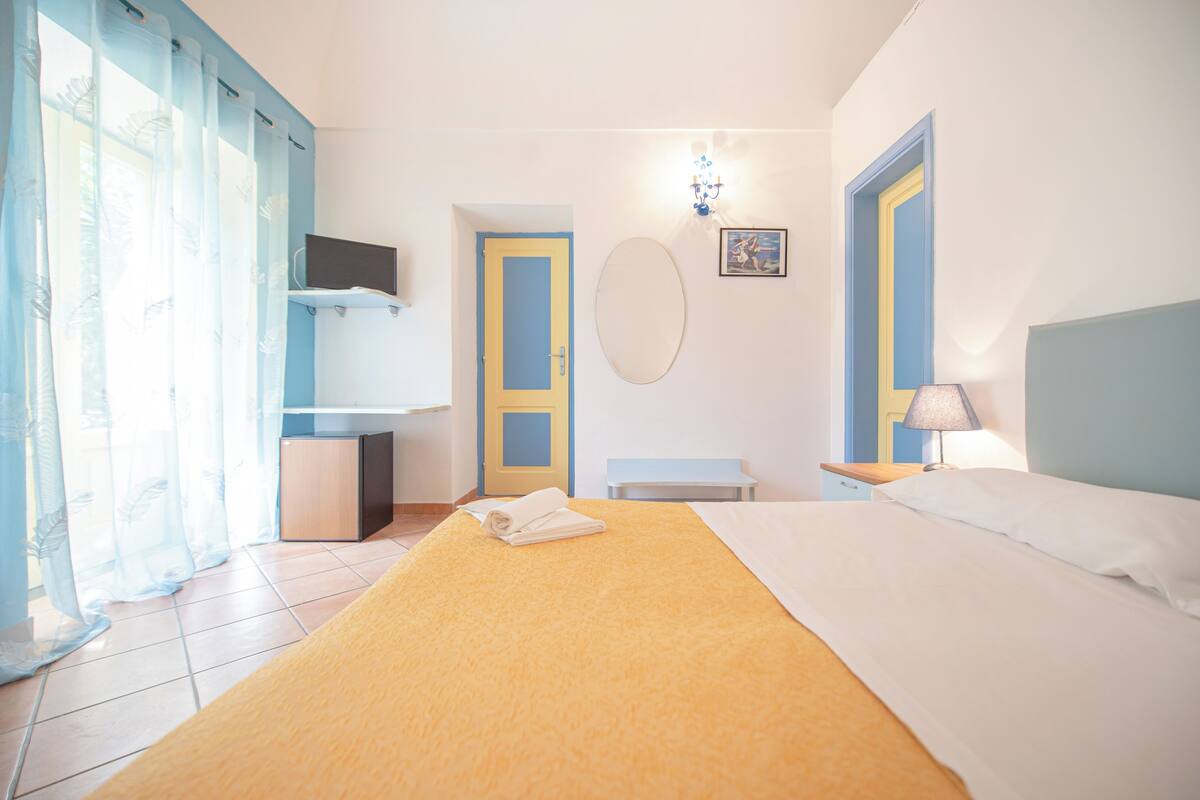 A hotel room with a bed, a bedside table, a lamp, a TV, and a bathroom with a shower curtain.